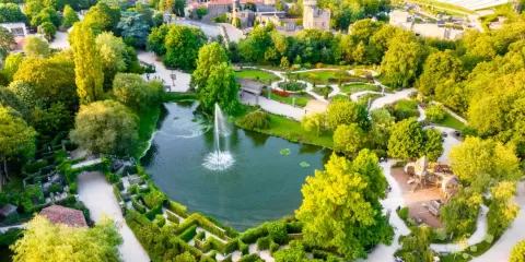 Photo des allées du parc du Puy du Fou verdoyantes ombragées autour d'un étang avec jet d'eau